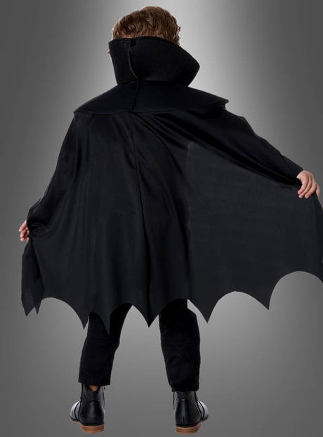 Ein Kind, das das Edler Dracula-Kostüm für Kinder trägt – mit schwarzem Umhang, hohem Kragen und gewellten Säumen –, steht mit dem Rücken zur Kamera und streckt die Arme aus wie ein klassischer Vampir.