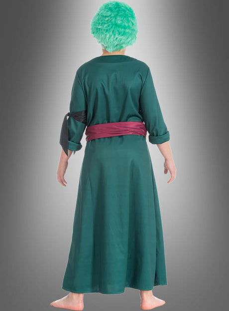 Eine Person steht barfuß mit dem Rücken zur Kamera vor einem grauen Hintergrund mit Farbverlauf und trägt ein Kostüm im Anime-Cosplay-Stil, das an das Zoro-Kostüm aus „One Piece“ erinnert, bestehend aus einem langen grünen Gewand, einer roten Schärpe und einer grünen Perücke.