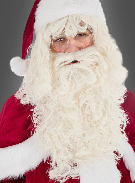Eine als Weihnachtsmann verkleidete Person, die einen roten Anzug und eine Brille trägt und das Set „Nikolausbart und Perücke Deluxe 40 cm“ mit weißem Lockenbart und Perücke trägt, posiert vor einem schlichten grauen Hintergrund.