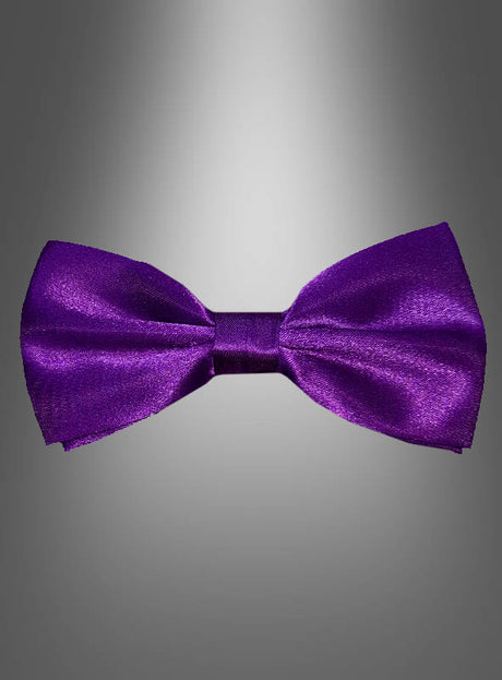 Eine glänzende, violette Deluxe-Satin-Fliege (13 x 6 cm) ist mittig auf einem grau verlaufenden Hintergrund platziert und bietet ein elegantes Accessoire für alle, die farbige Fliegen und einen raffinierten Stil schätzen.