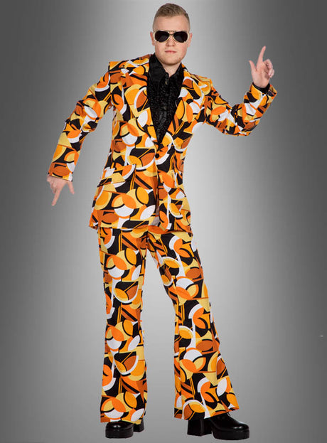 Eine Person, die den Retro-70er-Tanzanzug mit orangefarbenen Kreisen und Schlaghose, ein schwarzes Hemd, eine Sonnenbrille und Plateauschuhe trägt, posiert vor einem grauen Hintergrund – das perfekte Schlagerparty-Kostüm für jede disco-inspirierte Veranstaltung.