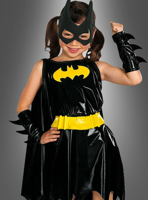 Ein junges Mädchen trägt das „Batgirl Deluxe“-Kinderkostüm, bestehend aus einem schwarzen Anzug mit gelbem Gürtel und Logo, einer passenden Maske und schwarzen Handschuhen, und steht selbstbewusst als Superheldin vor einem schlichten grauen Hintergrund.