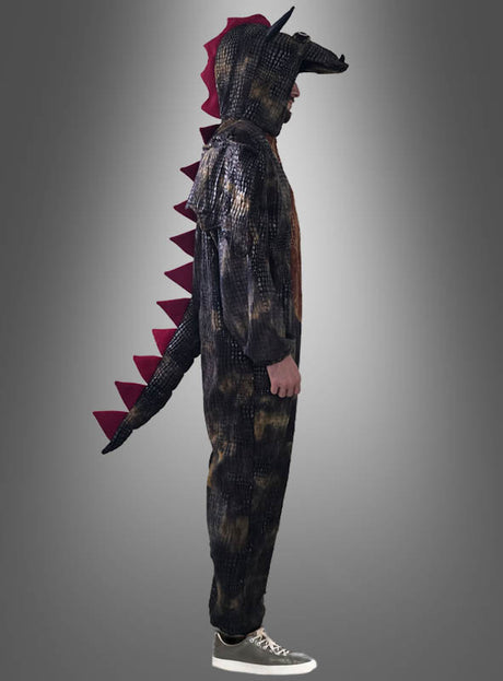 Eine Person, die den „Schwarzer Drachen Overall Erwachsene“ trägt – ein Ganzkörperkostüm mit Kapuze, Schwanz und roten Stacheln –, steht im Profil vor einem grauen Hintergrund.