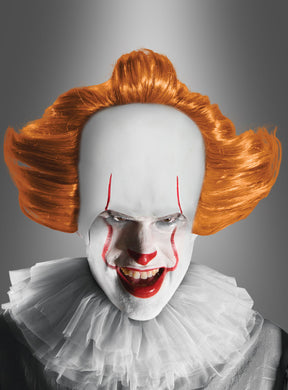Eine Person mit weißer Gesichtsbemalung, rotem Lippenstift, roter Nase und roten Augenbrauen, einer orangefarbenen Perücke im Pennywise-Stil, einem Rüschenkragen und einem grauen Outfit verkörpert vor einem grauen Hintergrund mit Farbverlauf ein bedrohliches Horrorclown-Kostüm.