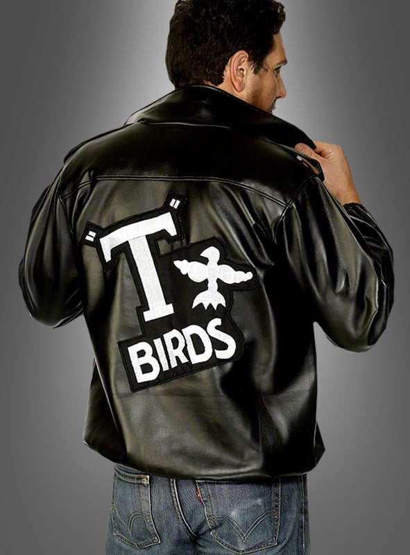 Vor einem grauen Hintergrund mit Farbverlauf steht ein Mann, der die T-Bird-Jacke „Grease 60er Jahre“ trägt, eine schwarze Jacke mit einem großen „T BIRDS“-Logo und einer Vogelgrafik auf dem Rücken. Dieses offizielle Lizenzprodukt ist das perfekte Kostüm für jeden „Grease“-Fan.