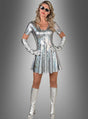 Eine Frau in einem schillernden Space-Disco-Kleid, dazu passende Handschuhe und kniehohe Stiefel, mit langen Haaren, Sonnenbrille und ausdruckslosem Gesicht, die vor einem grauen Hintergrund mit Farbverlauf steht.