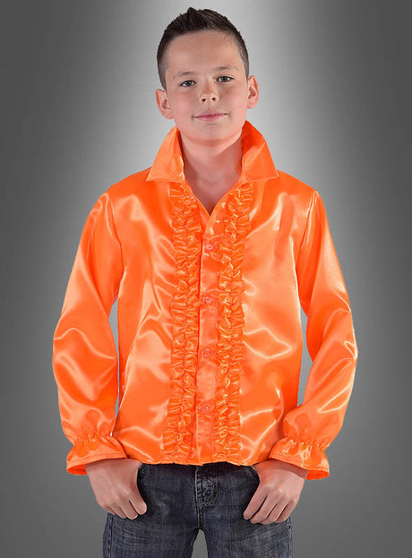 Ein junger Mensch trägt ein leuchtend orangefarbenes Rüschenhemd für Kinder in verschiedenen Farben, kombiniert mit Jeans, und steht vor einem grauen Hintergrund mit Farbverlauf – das ideale 70er-Jahre-Kostüm oder Disco-Party-Outfit für jede Feier im Retro-Stil.