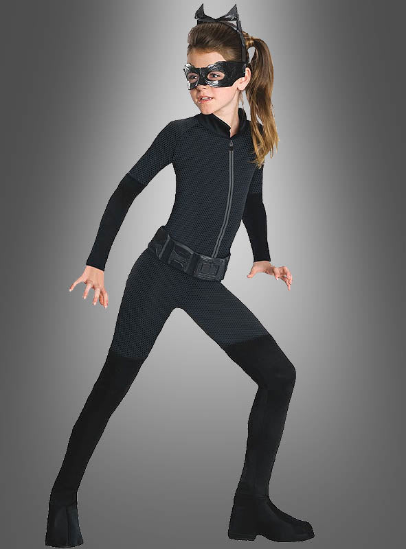 Ein Mädchen im Catwoman-Kinderkostüm – bestehend aus einem schwarzen Catsuit, original lizenzierten Katzenohren (Katzenohren-Stirnband), einer Augenmaske und schwarzen Stiefeln – nimmt vor einem grauen Hintergrund eine geduckte, kampfbereite Haltung ein und verkörpert damit perfekt den ikonischen Catwoman-Look.