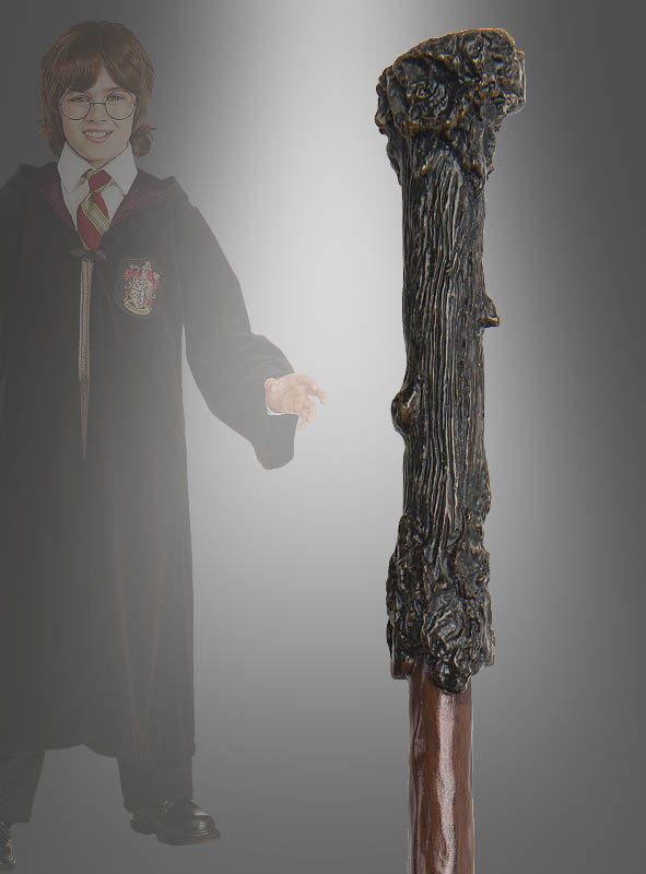 Eine Person in einer schwarzen Robe und einer gestreiften Krawatte – Teil eines authentischen Harry-Potter-Kostüms – steht lächelnd da, während im Vordergrund ein hölzerner, strukturierter „Deluxe Zauberstab Harry Potter“ scharf im Bild zu sehen ist.