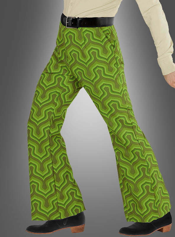 Eine Person, die die „Retro Hose Herren grün“ mit grünem Retro-Muster trägt, kombiniert mit einem beigen Hemd, einem schwarzen Gürtel und schwarzen Schuhen, geht vor einem grauen Hintergrund mit Farbverlauf.