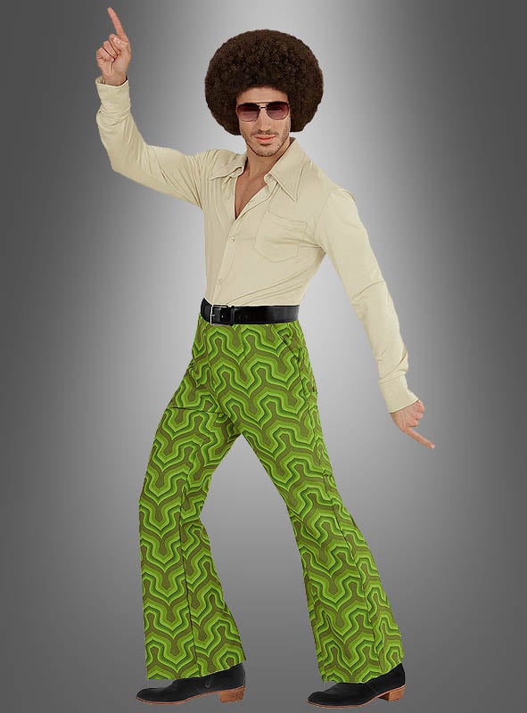 Ein Mann in einem cremefarbenen Hemd, einer grünen Herrenhose im Retro-Stil mit Retro-Muster, einer Sonnenbrille und einer Afro-Perücke nimmt vor einem grauen Hintergrund mit Farbverlauf eine klassische Disco-Tanzpose ein.