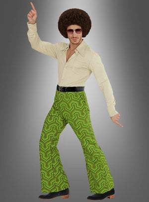 Ein Mann in einem cremefarbenen Hemd, einer grünen Herrenhose im Retro-Stil mit Retro-Muster, einer Sonnenbrille und einer Afro-Perücke nimmt vor einem grauen Hintergrund mit Farbverlauf eine klassische Disco-Tanzpose ein.