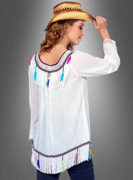 Eine Person in einem weißen, mit bunten Federn verzierten Oberteil mit Fransen und einem Cowboyhut, von hinten vor einem grauen Hintergrund gesehen – sie verkörpert perfekt den Bohemian-Charme der „Hippie-Tunika mit Federn und Fransen“.