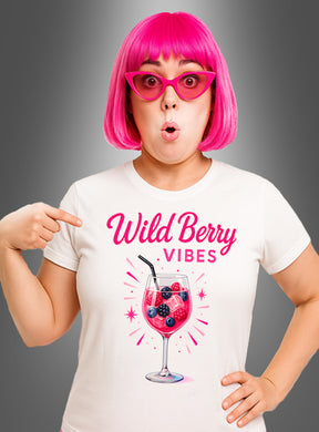 Eine Frau mit einer rosa Perücke und einer Sonnenbrille zeigt auf ihr Cocktail-T-Shirt „Wild Berry Vibes“, auf dem der Schriftzug „Wild Berry Vibes“ und die Abbildung eines Lillet Wild Berry-Drinks in einem Weinglas vor einem grauen Hintergrund mit Farbverlauf zu sehen sind.