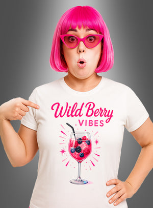 Eine Frau mit einer rosa Perücke und einer Sonnenbrille zeigt auf ihr Cocktail-T-Shirt „Wild Berry Vibes“, auf dem der Schriftzug „Wild Berry Vibes“ und die Abbildung eines Lillet Wild Berry-Drinks in einem Weinglas vor einem grauen Hintergrund mit Farbverlauf zu sehen sind.