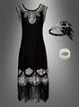 XXL-Kostüm im Stil der 20er Jahre mit Accessoires „Tatiana“: Elegantes schwarzes Charleston-Kleid im Stil der 1920er Jahre mit silbernen Pailletten, Fransenbesatz und passenden Accessoires wie Stirnband, Armband und Feder-Haarschmuck auf grauem Hintergrund – perfekt als Paillettenkleid in Übergröße für stilvolle Flapper-Looks.