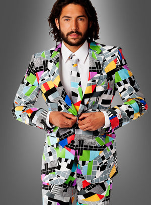 Ein Mann, der den „Deluxe Testbild Anzug“ von OppoSuits trägt – einen farbenfrohen Anzug mit geometrischen Mustern und einer passenden Krawatte –, steht vor einem schlichten grauen Hintergrund und knöpft seine Jacke zu; das perfekte Outfit für jede 70er-Jahre-Mottoparty.