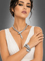Eine Frau in einem weißen, ärmellosen Kleid trägt das „Schlangen-Schmuck-Set mit Strass“, bestehend aus einer auffälligen silbernen Halskette und einem Armband mit Schlangenmotiv, die mit schimmernden Kristallen verziert sind, während sie mit vor der Brust verschränkten Armen vor einem grauen Hintergrund mit Farbverlauf posiert.