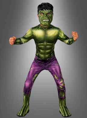 Ein Kind im „Hulk Deluxe“-Kinderkostüm – mit grüner Maske, muskulöser Brust und zerrissener lila Hose – steht mit geballten Fäusten vor einem grauen Hintergrund.
