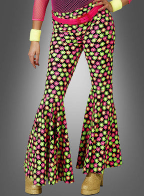 Eine Person, die die „Elastische Schlaghose mit Blumenmuster in Neonfarben“, goldene Plateauschuhe, Accessoires in Neonfarben und einen rosa Gürtel trägt, posiert vor einem grauen Hintergrund.