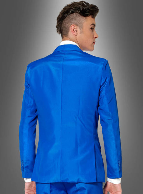 Eine Person mit kurzen braunen Haaren, die einen blauen Anzug der Marke „Anzugmeister“ trägt, steht mit dem Rücken zur Kamera vor einem grauen Hintergrund mit Farbverlauf.