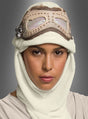 Eine Person trägt die „Star Wars Rey Brille und Haube für Erwachsene“ mit einem cremefarbenen Kopftuch und einer Brille im Vintage-Stil auf der Stirn und posiert mit ausdruckslosem Gesicht vor einem grauen Hintergrund.