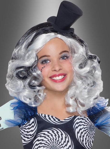 Ein Mädchen, das die „Frankie Stein Monster High“-Kinderperücke mit schwarz-weißen Locken trägt, dazu einen kleinen Zylinder und ein „Freak du Chic“-Kostüm mit wirbelnden Mustern, lächelt vor einem grauen Hintergrund mit Farbverlauf in die Kamera.