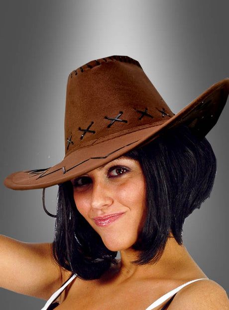 Eine Frau mit kurzen dunklen Haaren, die den Cowboy-Hut für Damen und Herren in Braun und ein weißes Oberteil trägt, lächelt sanft vor einem grau verlaufenden Hintergrund – ein ideales Accessoire für ein stilvolles Westernkostüm.