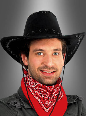 Ein Mann, der den „Cowboy Hut für Damen und Herren“ in Schwarz trägt und ein rotes Bandana um den Hals gebunden hat, vor einem neutralen, grau verlaufenden Hintergrund.