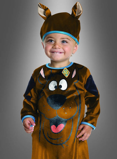 Ein kleines Kind, das das Scooby-Doo-Hunde-Kinderkostüm mit einer passenden Mütze mit Ohren trägt und lächelnd vor einem grauen Hintergrund mit Farbverlauf steht.