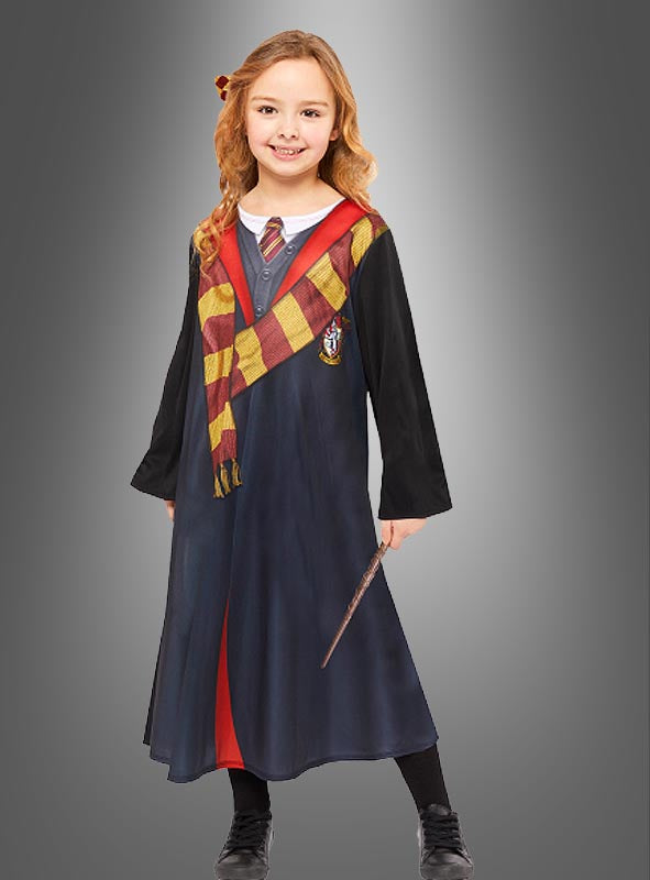 Ein Kind, das das bedruckte Hermine-Granger-Kostüm-Set trägt – bestehend aus einer schwarzen Gryffindor-Robe, einem dazu passenden rot-gelben Schal und einem Zauberstab in der Hand –, steht lächelnd vor einem grauen Hintergrund und ist damit das perfekte Harry-Potter- oder Hermine-Granger-Kostüm für junge Fans.