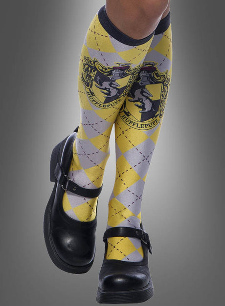 Ein Paar gelbe Hufflepuff-Kniestrümpfe aus der Harry-Potter-Reihe mit einem gelb-grauen Argyle-Muster und dem ikonischen Hufflepuff-Wappen passt perfekt zu jeder Hogwarts-Schuluniform, wenn man sie mit klassischen schwarzen Mary-Jane-Schuhen kombiniert.