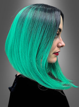 Frau im Profil mit glattem, schulterlangem Haar in leuchtendem Grün mit schwarzen Ansätzen, die ein schwarzes Oberteil trägt, vor einem schlichten grauen Hintergrund. Dieser auffällige Look besticht durch die „Zwei-Ton-Farbe-Perücke Lilia“, die mit einem trendigen zweifarbigen Farbverlauf gestylt ist.