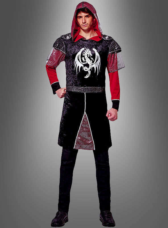 Ein Mann, der das „Drachenritter“-Kostüm für Herren trägt – ein mittelalterlich anmutendes schwarz-rotes Outfit mit Kapuze, silbernen Kettenverzierungen und einem weißen Drachenemblem auf der Brust –, steht vor einem grauen Hintergrund mit Farbverlauf.