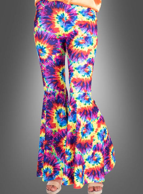 Eine Person, die eine „Hippie Batik Schlaghose für Damen“ – eine klassische Hose aus den 70er Jahren – trägt, kombiniert mit offenen Schuhen, steht vor einem neutralen grauen Hintergrund.