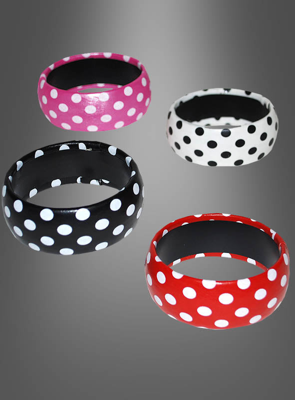 Vier „Armreif 50er Pünktchen“-Armreifen in Rosa, Weiß, Schwarz und Rot – jeweils mit klassischen weißen Polka-Punkten verziert – verkörpern den verspielten Geist der Rock’n’Roll-Accessoires der 1950er Jahre. Diese stilvollen Armreifen werden vor einem grauen Hintergrund mit Farbverlauf präsentiert.