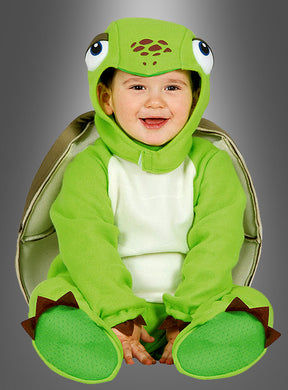 Auf dem Bild ist ein fröhliches Kind zu sehen, das vor einem grauen Hintergrund sitzt und das „Baby-Schildkröte-Kostüm“ trägt – ein entzückendes grünes Schildkrötenkostüm mit einer Kapuze mit großen Comic-Augen, einem Panzer auf dem Rücken und flossenförmigen Füßen.