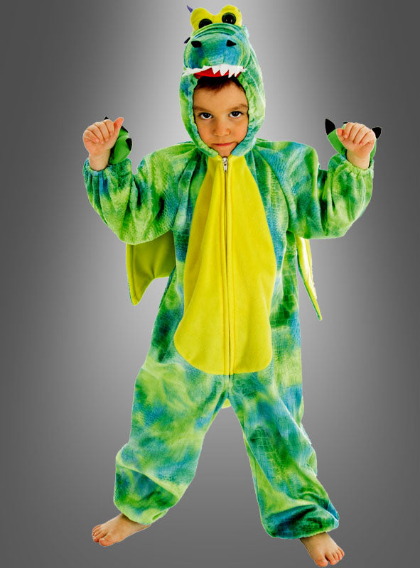 Ein Kind, das das „Dinosaurier-Kinderkostüm Kleiner Drache“ in den Farben Grün und Blau trägt, steht vor einem grauen Hintergrund, hat die Arme erhoben und blickt in die Kamera.