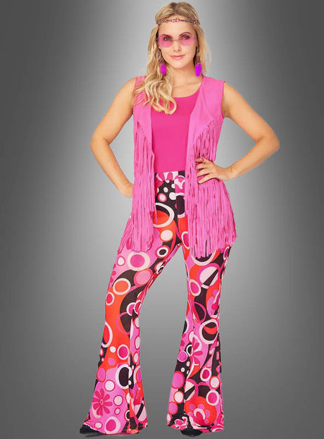 Eine Person trägt das „60er-Jahre-Hippie-Kostüm-Set Pink Dream“, bestehend aus einem rosa Stirnband, einer rosa Weste mit Fransen, einem rosa Oberteil und einer bunt gemusterten Schlaghose vor einem grauen Hintergrund mit Farbverlauf – ideal als 60er-Jahre-Damenkostüm oder als farbenfrohes Flower-Power-Kostüm für Ihre nächste Party.