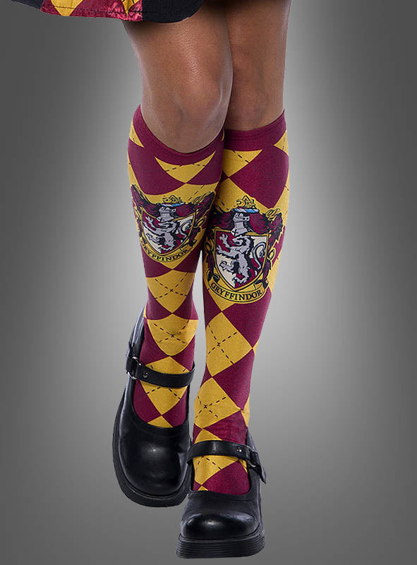 Eine Person, die schwarze Schuhe und die Gryffindor-Kniestrümpfe „Harry Potter rot-gelb“ – rot-gelbe Argyle-Kniestrümpfe mit dem Gryffindor-Wappen – trägt, die an eine Hogwarts-Schuluniform erinnern, steht vor einem grauen Hintergrund.