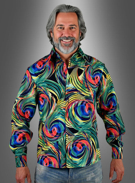 Ein Mann mit grauen Haaren und Bart trägt das „Buntes 70er Hemd Wirbelwind“ – ein farbenfrohes Hemd mit abstrakten Mustern und Knöpfen – sowie blaue Jeans und steht vor einem grauen Hintergrund mit Farbverlauf – perfekt gekleidet für ein Hippie-Festival oder eine Schlagerparty.