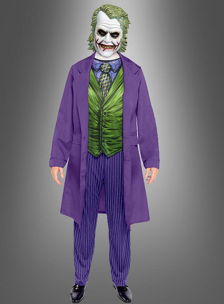 Eine Person, die das „Original Comic Joker Kostüm Herren“ trägt – bestehend aus einem violetten Mantel, einer grünen Weste, einer gemusterten Krawatte, einer gestreiften Hose, schwarzen Schuhen und einer Joker-Maske, die von der DC-Comic-Figur inspiriert ist –, steht vor einem grauen Hintergrund mit Farbverlauf.