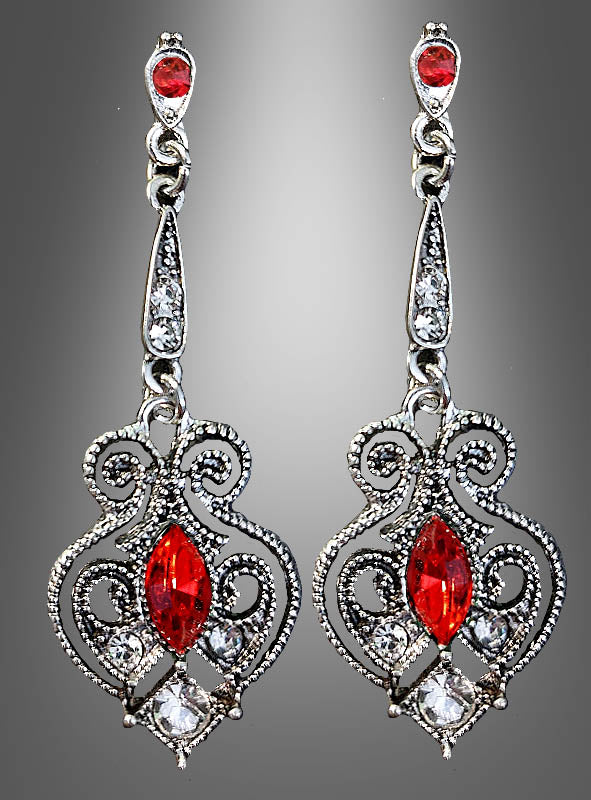 Ein Paar Ohrringe im Antik-Stil mit Edelsteinen, gefertigt aus kunstvoll verziertem Silber mit roten und klaren Edelsteinen, mit filigranen Wirbelmustern und hängenden Elementen, präsentiert vor einem grauen Hintergrund mit Farbverlauf.