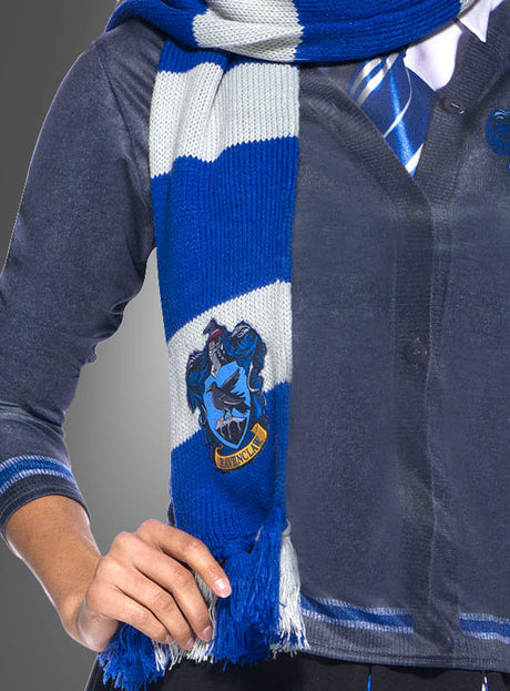 Person, die einen blauen Ravenclaw-Schal aus der Harry-Potter-Reihe mit blauen und weißen Streifen und einem Ravenclaw-Wappen trägt, dazu ein blaues Hemd und eine dazu passende Krawatte – fotografiert von den Schultern bis zur Taille. Dieses Harry-Potter-Kostümzubehör ist perfekt, um deinen Hausstolz zu zeigen.