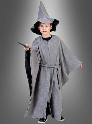 Ein Kind, das die „Grauer Zauberer“-Kinderrobe mit Hut trägt – komplett mit spitzem Hut und Robe –, hält einen Zauberstab in der Hand und steht vor einem grau abgestuften Hintergrund.
