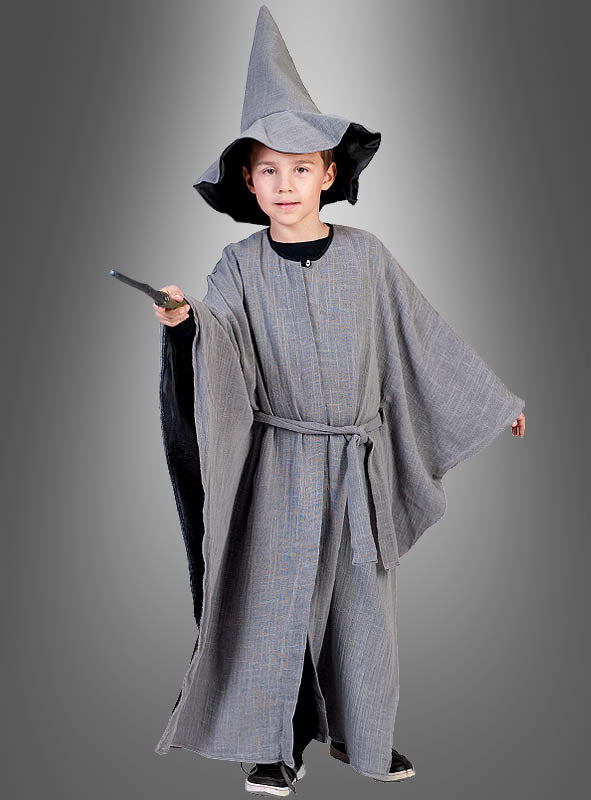 Ein Kind, das die „Grauer Zauberer“-Kinderrobe mit Hut trägt – komplett mit spitzem Hut und Robe –, hält einen Zauberstab in der Hand und steht vor einem grau abgestuften Hintergrund.
