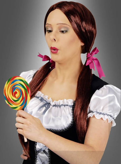 Eine Frau mit langen braunen Haaren, die zu zwei Zöpfen geflochten sind, trägt die Perücke „Zopfperücke mit zwei Zöpfen“, kombiniert sie mit einem mit rosa Bändern verzierten Kostümkleid und schaut überrascht, während sie einen großen Regenbogen-Lutscher in der Hand hält.