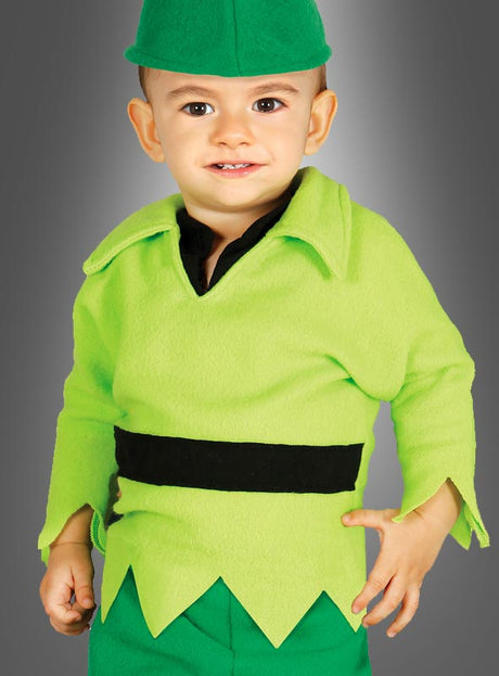 Ein Kleinkind mit einer grünen Mütze und einem leuchtend grünen Outfit mit schwarzem Gürtel steht lächelnd vor einem grauen Hintergrund – ein entzückendes „Kleiner Peter“-Märchenkostüm für Jungen, perfekt für jeden märchenhaften Anlass.
