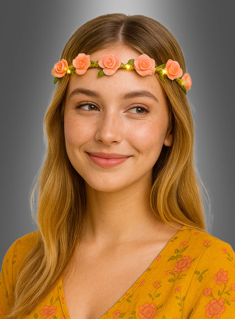 Eine junge Frau mit langen blonden Haaren posiert vor einem grauen Hintergrund mit Farbverlauf. Sie trägt ein gelbes Oberteil mit Blumenmuster und den Blumen-Haarkranz „Rosen mit LED-Licht“.