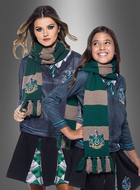 Zwei Mädchen in von Slytherin inspirierten Outfits und mit dem grünen Slytherin-Schal aus Harry Potter stehen vor einem grauen Hintergrund mit Farbverlauf und präsentieren damit das perfekte Kostümzubehör für jeden Harry-Potter-Fan.